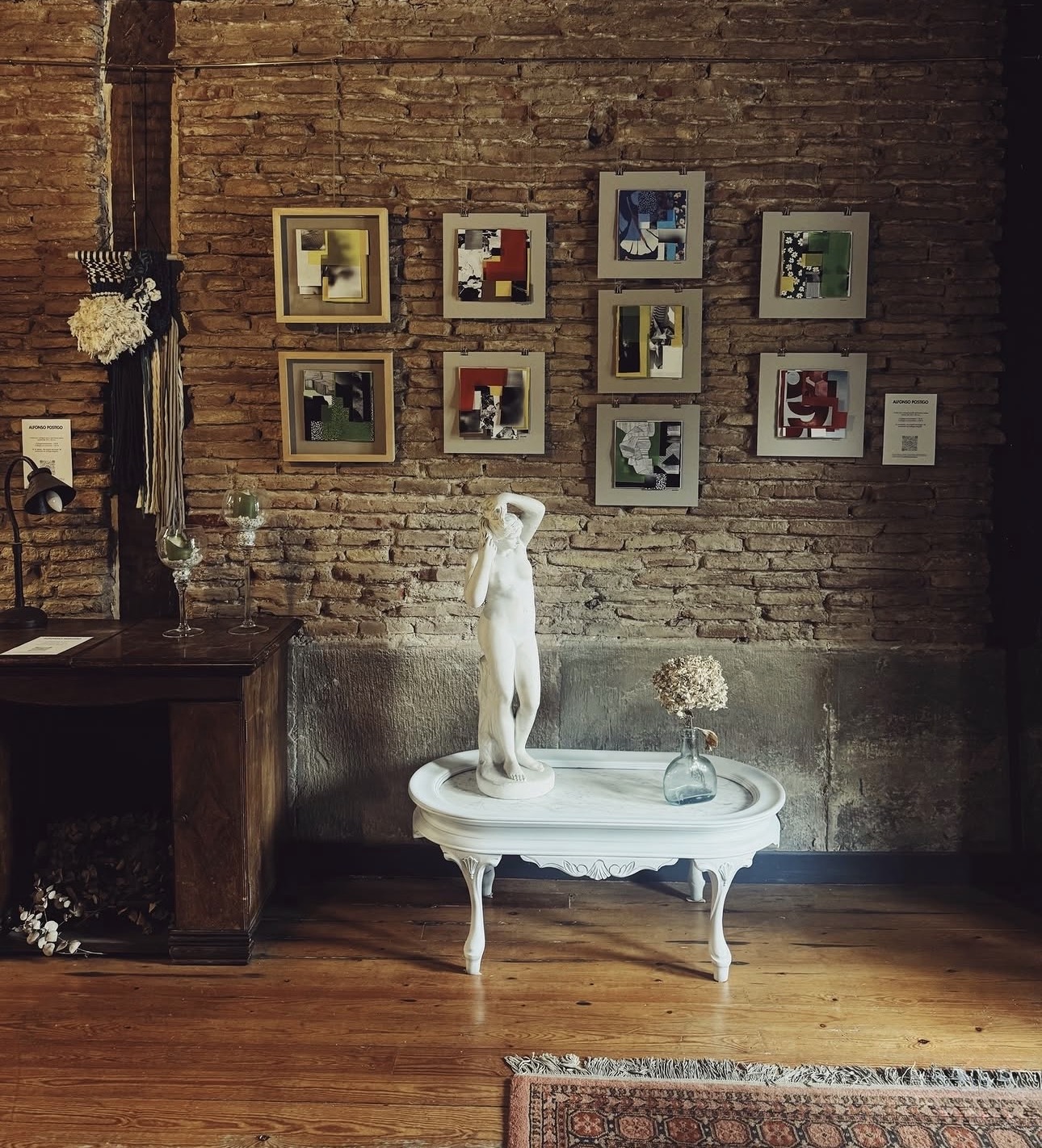 Pared de ladrillo con una serie de collages enmarcados sobre una mesa blanca